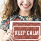 Symbolbild Ideenreich: lächelnde Frau hält Schild mit der Beschriftung "keep calm" in der Hand